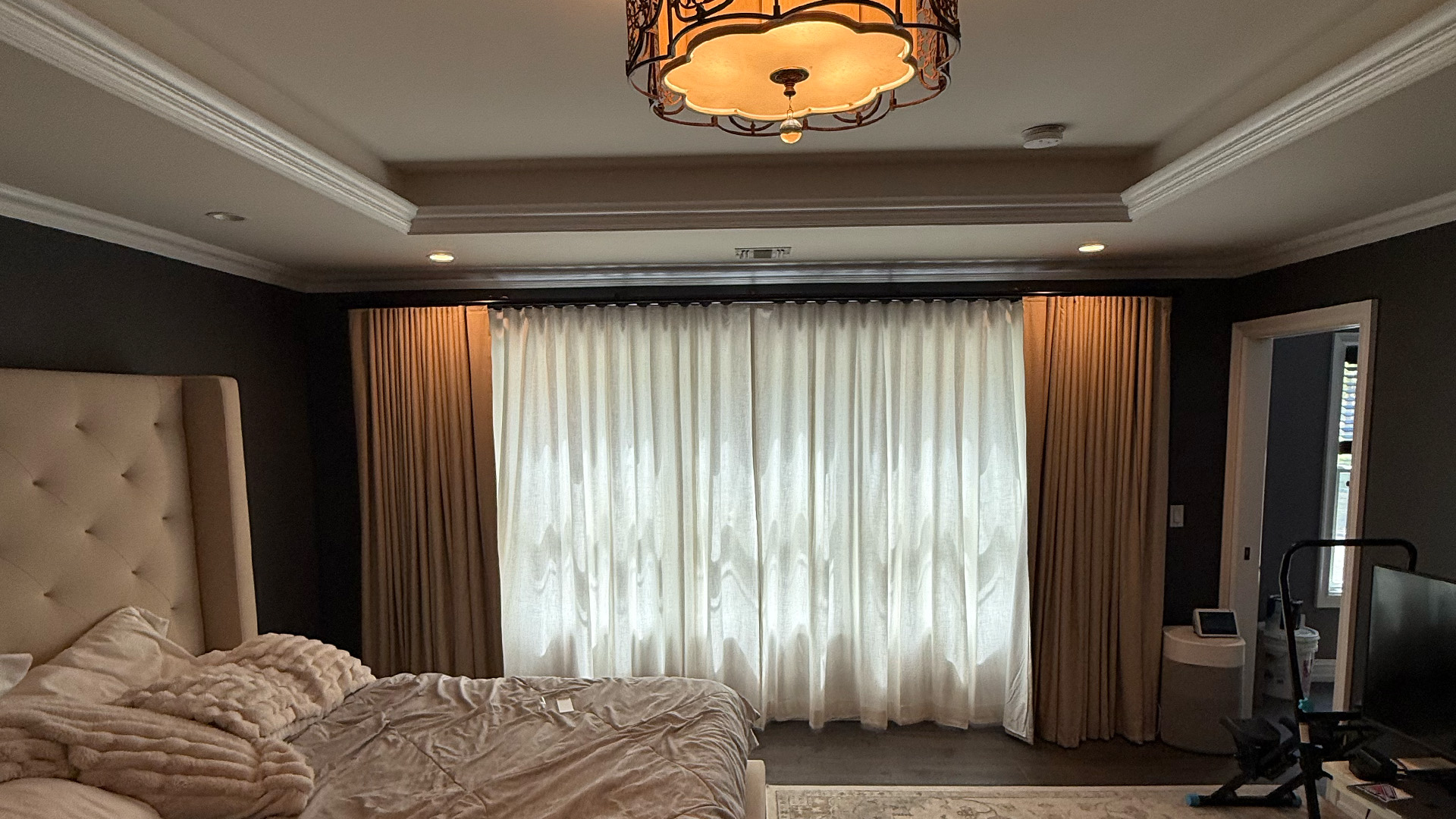 Bedroom with Roman shades and drapery framing an arched window.